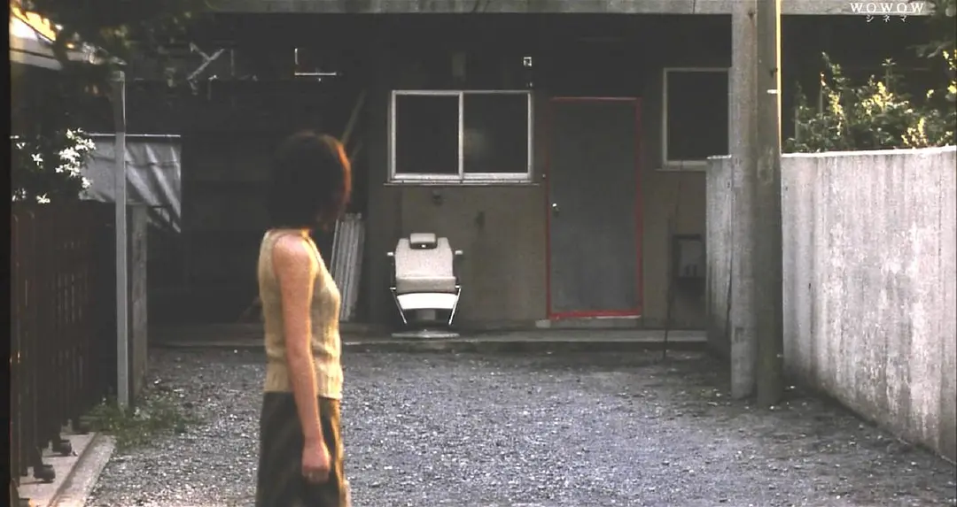 A doorway sealed with red tape in the film Kairo, seen across an empty gravel yard